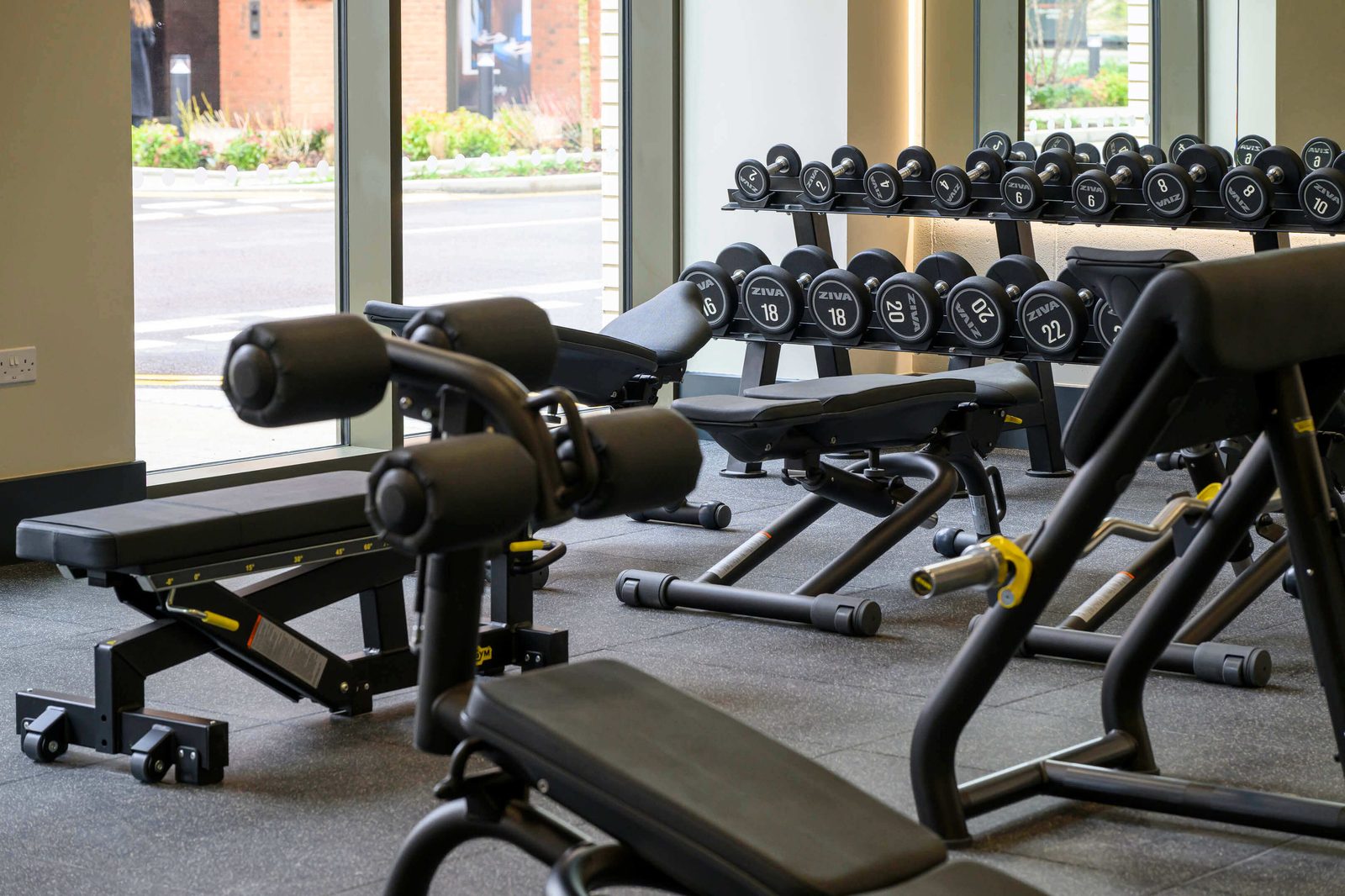 Lombard Square Plumstead SE28 residents gym free-weights area with dumbbell racks and adjustable benches alongside floor-to-ceiling windows